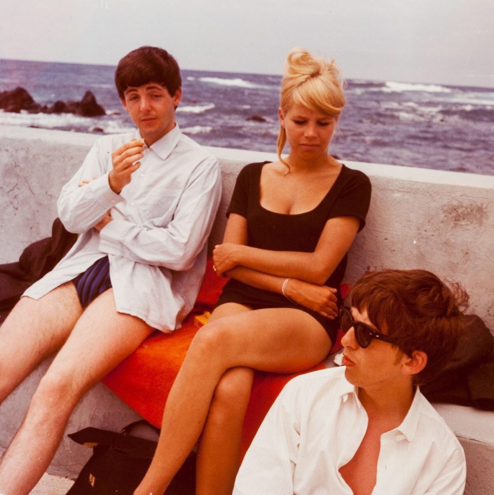 Na zdjęciu widzimy siedzących na bulwarze dwóch muzyków i blondynkę. Jeden muzyk w okularach przeciwsłonecznych patrzy się w bok, zaś drugi muzyk pali papierosa.