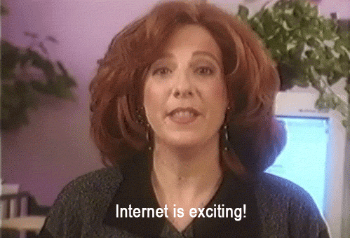 Biała, podekscytowana kobieta,która jest ubrana w czarną elegancką koszule informuje o wartości internetu. W tle widać kwiatki w doniczkach, różową ściane i monitor.