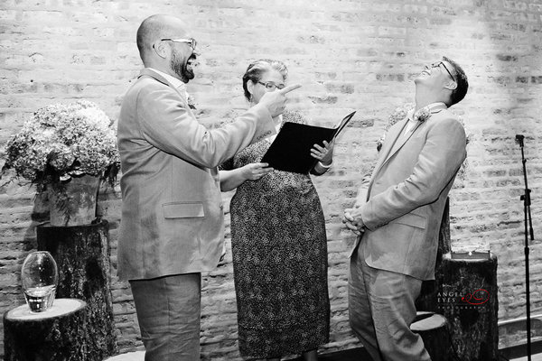 Czarnobiałą fotografia dwoch mezczyzn bioracych własnie ślub. Nie widać po nich uczucia stresu, są wyraźnie w doskonałych humorach. Obydwaj są roześmiani jakby dopiero co któryś skonczył opowiadać dowcip.