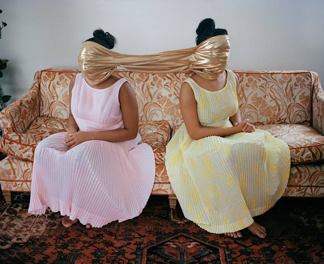 Dwie kobiety siedzące w sukienkach na kanapie z zakrytymi jedną chustą twarzami