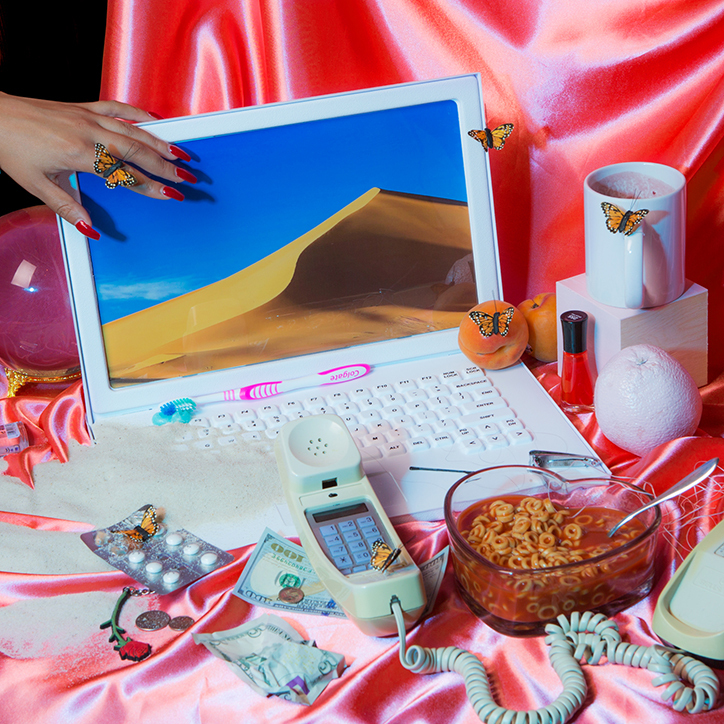 Porozkładane przedmioty: komputer, telefon, kubek, bibeloty na różowym kawałku satyny