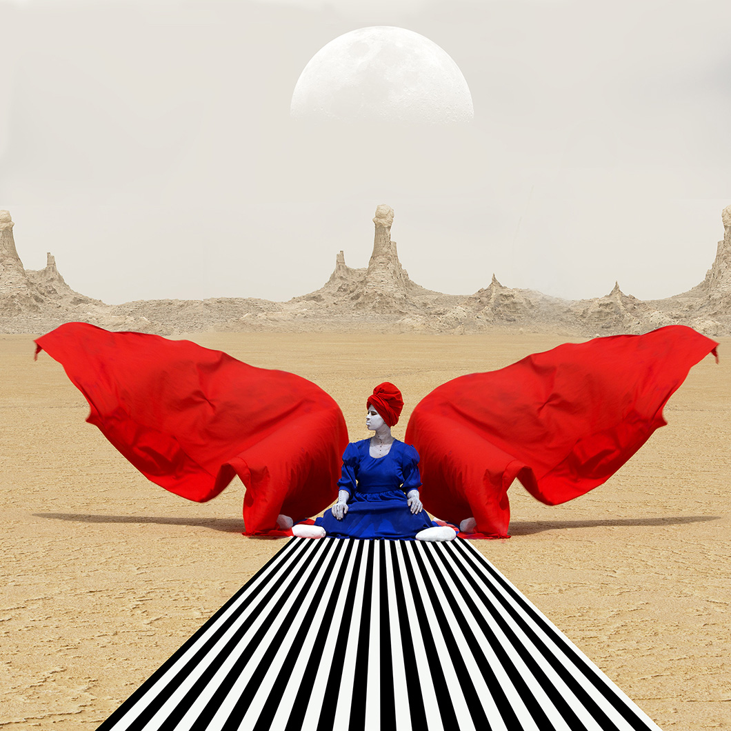 Zdjęcie przedstawia kobietę ubraną w niebieską suknie i czerwony turnab siedzącą przed czarno-białym dywanem. Obraz jest symetryczny po obu jej stronach widać czerwony materiał przypominający skrzydła. W tle widnieje pustynia i wielki półksiężyc