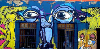 Kolorowy mural przedstawiający twarz - oczy, nos, usta, umieszczone między oknami budynku