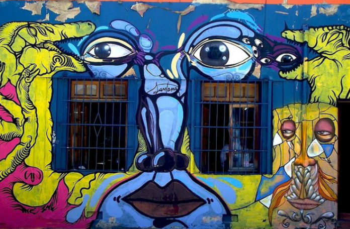 Kolorowy mural przedstawiający twarz - oczy, nos, usta, umieszczone między oknami budynku
