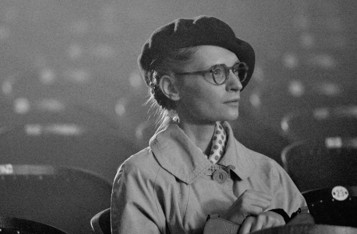 Czarno-białe zdjęcie kobiety siedzącej w kinie w płaszczu i berecie
