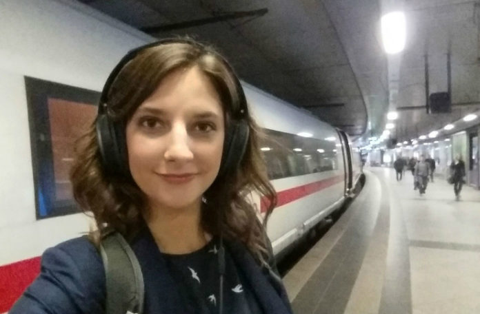 Brutnetka ze słuchawkami na głowie stojąca na tle pociągu