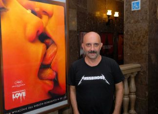 Łysy mężczyzna w czarnej koszulce na tle plakatu do filmu "Love"