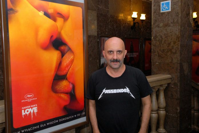 Łysy mężczyzna w czarnej koszulce na tle plakatu do filmu 