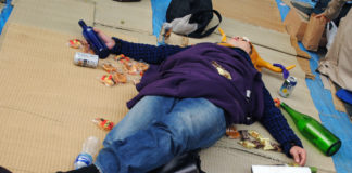 Kobieta leżąca na podłodze pełnej śmieci, butelek