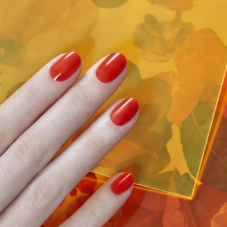 kobiece palce z umalowanymi paznokciami w kolorze pomarańczowym