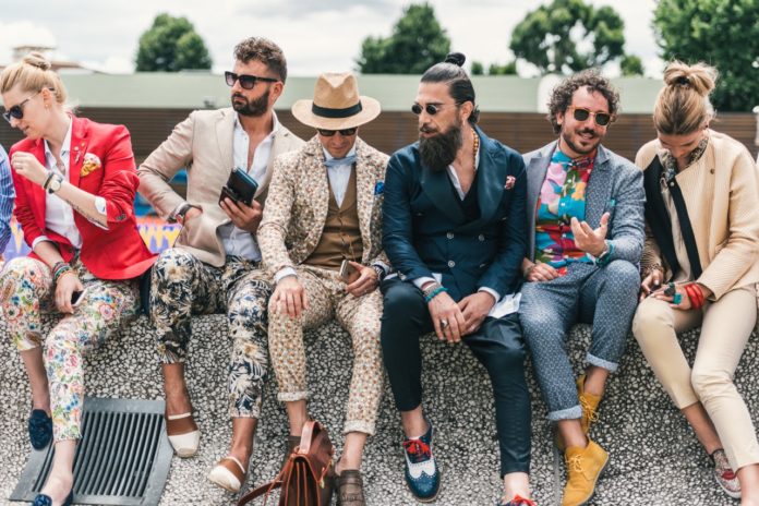 Grupa facetów w kolorowych garniturach siedzi na murku