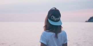 Dziewczyna w czapce z daszkkiem i białej bluzce stoi odwrócona w stronę morza