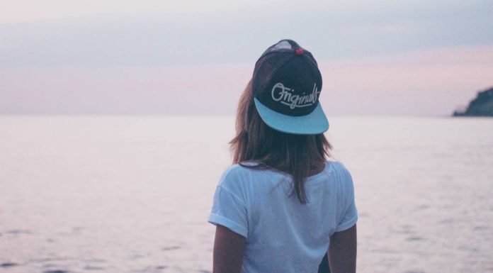 Dziewczyna w czapce z daszkkiem i białej bluzce stoi odwrócona w stronę morza