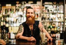 Mężczyzna z brodą i tatuażami na tle baru