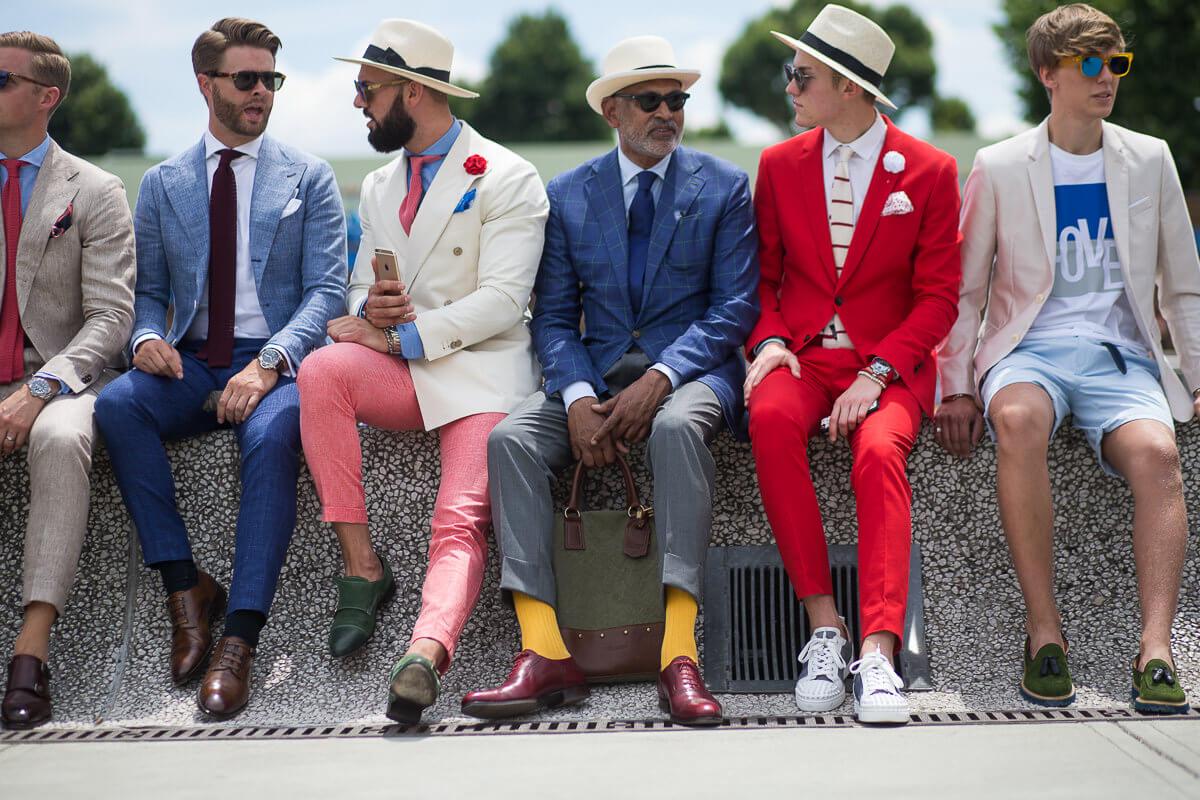 Grupa facetów w kolorowych garniturach siedzi na murku
