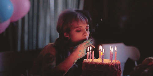 Dziewczyna z tatuażami i kolorowymi włosami odpala papierosa od świeczki z tortu