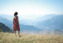 Dziewczyna w czerwonej sukience na łące patrzy na góry