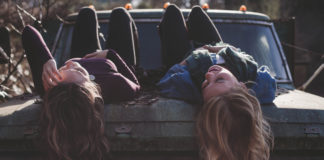 Dwie dziewczyny z długimi włosami leżą na masce samochodu