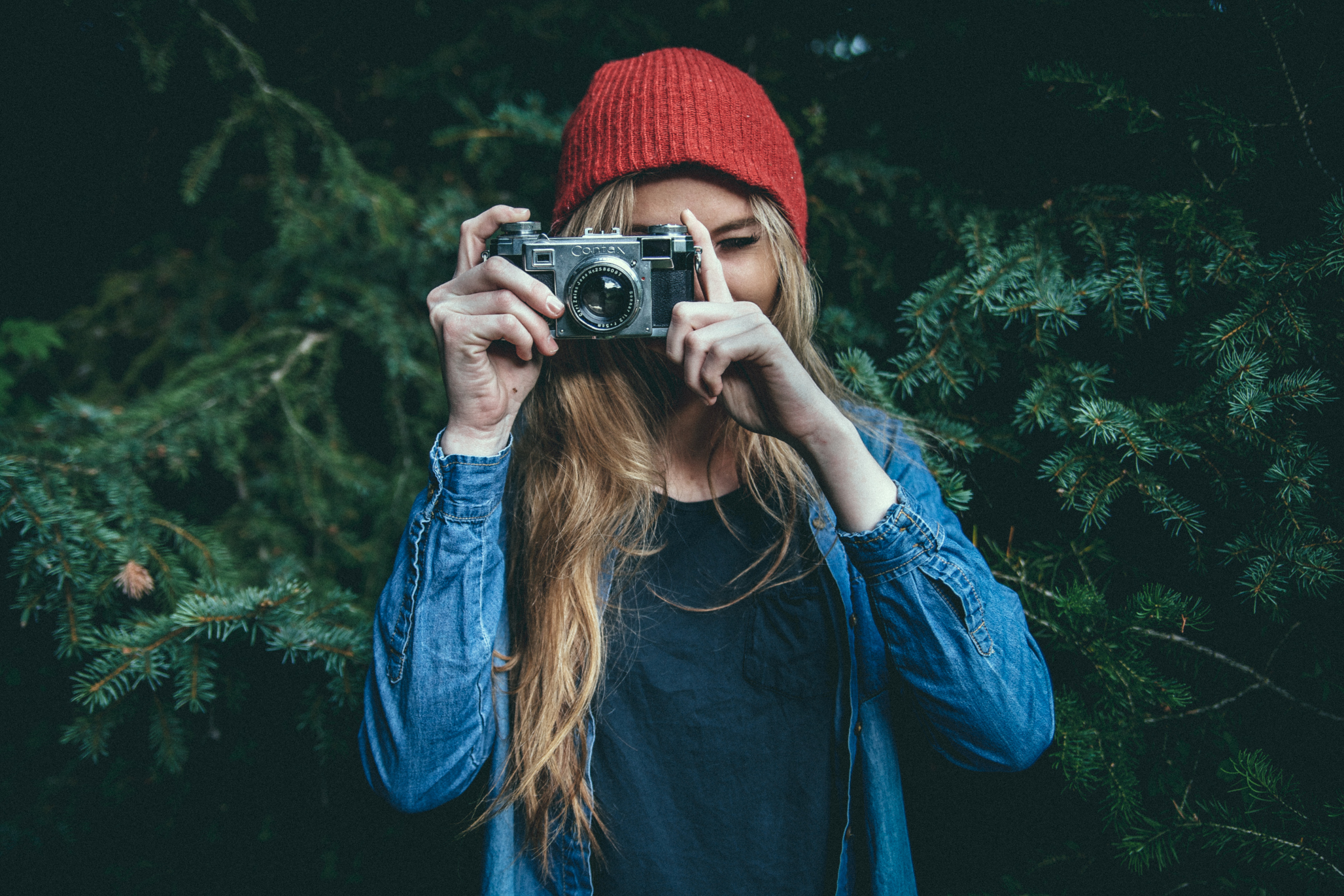 Dziewczyna ubrana na niebiesko w czerwonej czapce robi zdjęcie aparatem