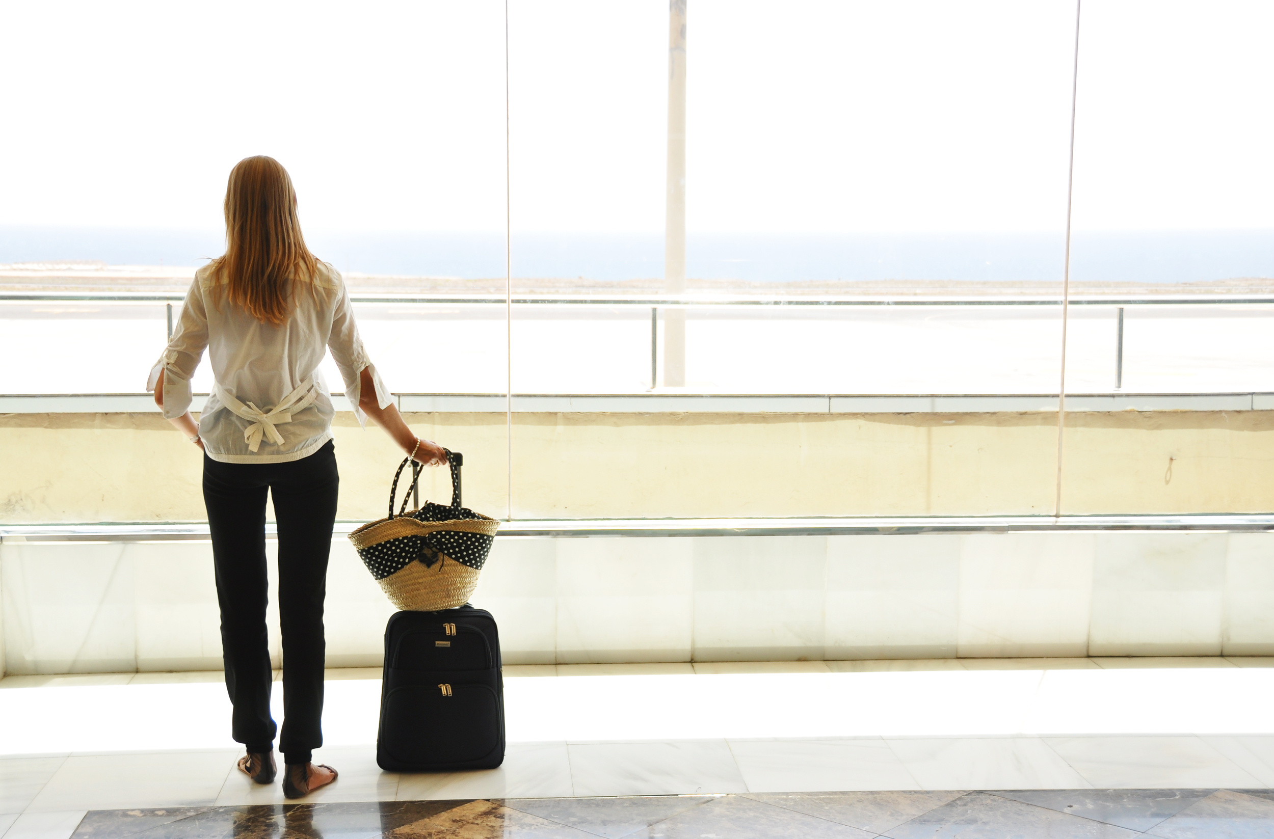 Kobieta w białej bluzce i czzarnych spodniach z walizką na lotnisku