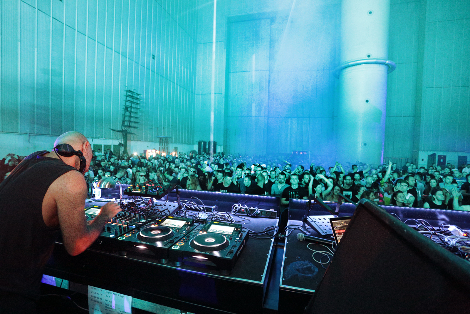 DJ i tłum imprezujących ludzi na błękitnym tle wielkiej hali