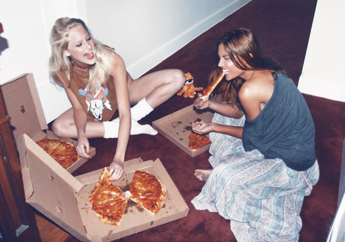 Blondynka i brunetka jedzą pizzę na podłodze