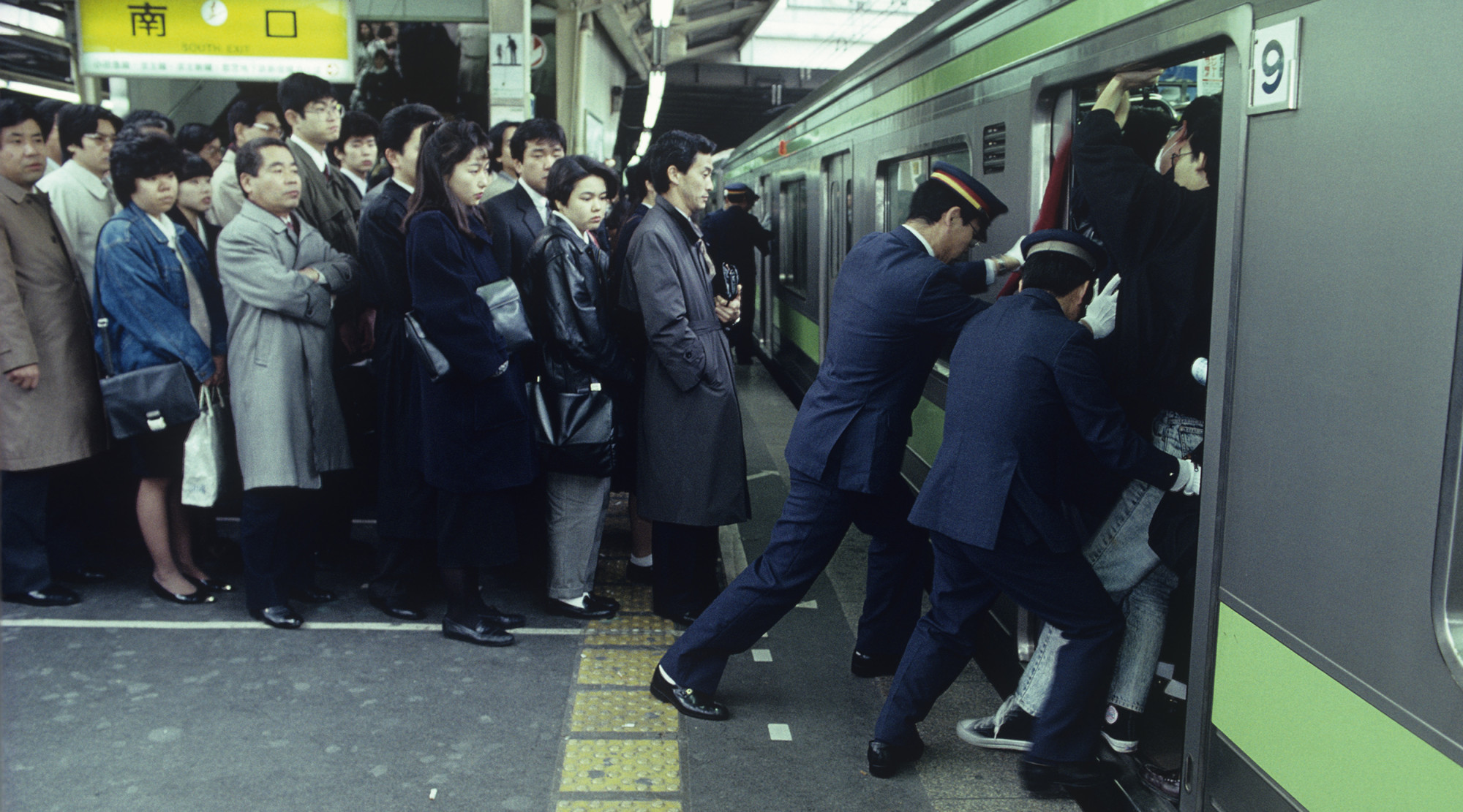 Tłum ludzi w japońskim metrze, konduktorzy upychają pasażerów