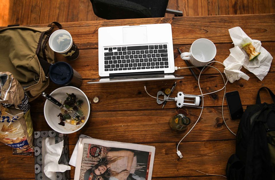 Nieuporządkowane biurko na którym jest miska po jedzeniu, laptop, ogryzek i kubek