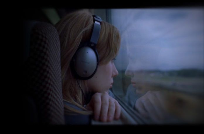Dziewczyna ze słuchawkami na uszach patrzy przez okno w pociągu