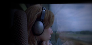 Dziewczyna ze słuchawkami na uszach patrzy przez okno w pociągu