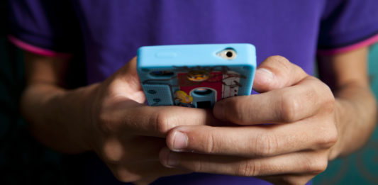 Ręce chłopaka trzymającego telefon w kolorowej obudowie