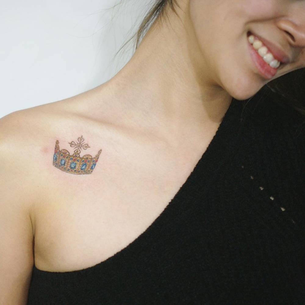 Kobieta ubrana na czarno z tatuażem korony na obojczyku