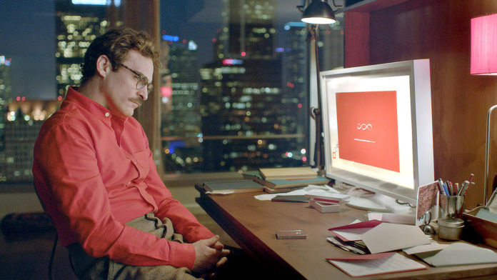 Mężczyzna w czerwonej koszuli i okularach siedzi przed komputerem