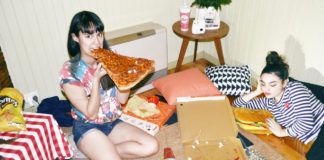 Dwie dziewczyny siedzą w pokoju na podłodze i jedzą pizzę