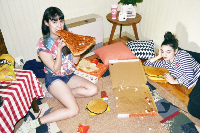 Dwie dziewczyny siedzą w pokoju na podłodze i jedzą pizzę