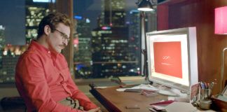 Mężczyzna w czerwonej koszuli i okularach siedzi przed komputerem