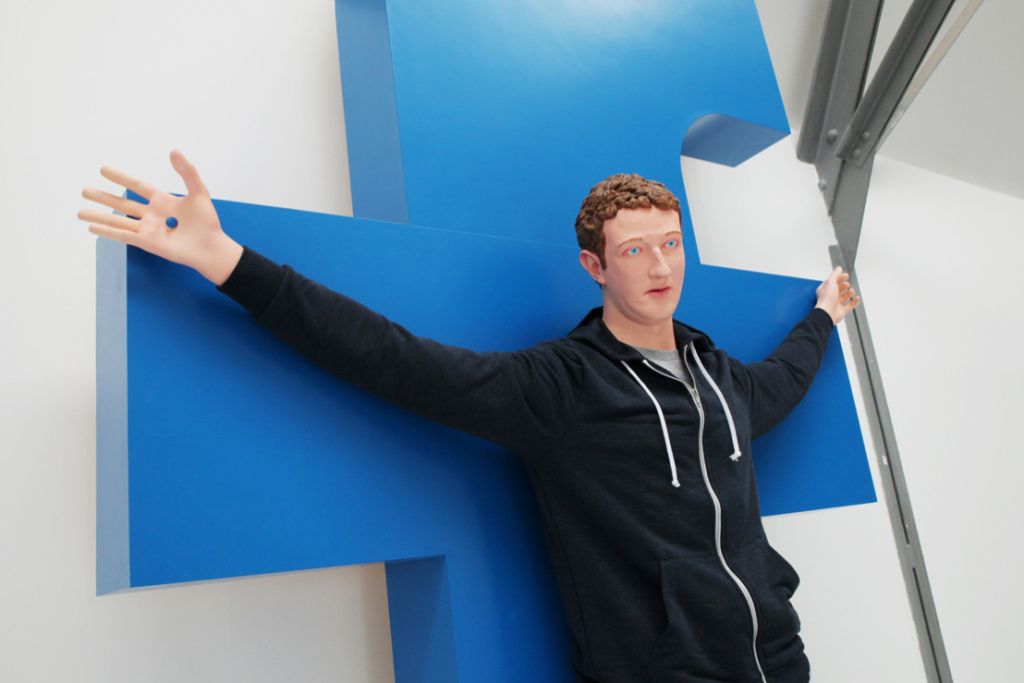 Rzeźba przedstawiająca mężczyznę w bluzie wiszącego na niebieskiej literze "F"