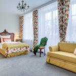 Pokój z dużym podwójnym łóżkiem, żółto-pomarańczową kanapą i zabytkową komodą