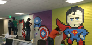 Pracownicy biura przyklejący do ścian samoprzylepne karteczki, które tworzą obrazek supermana