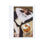 Polaroid z dziewczyną leżącą na podłodze w czarnych majtkach i jasnej z bluzie z pizzą z boku