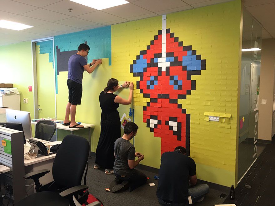 Pracownicy biura przyklejący do ścian samoprzylepne karteczki, które tworzą obrazek Spidermana