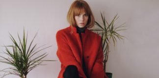 Rudowłosa dziewczyna z grzywką w czerwonym płaszczu siedzaca na szafce