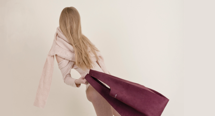 Dziewczyna w różowym narzuconym na ramiona swetrze, machająca bordową torbą