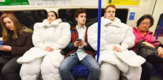 Dwoje ludzi, kobieta i mężczyzna siedzacy w metrze ubrani w strój, który wygląda jak kołdra