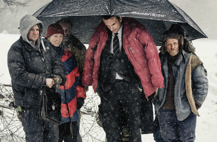Grupa ludzi ubrana w kurski, stojąca pod dużym parasolem, dookoła pada śnieg