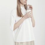 Dziewczyna ubrana w białą bluzkę i kremową spódnicę pije mleko z butelki