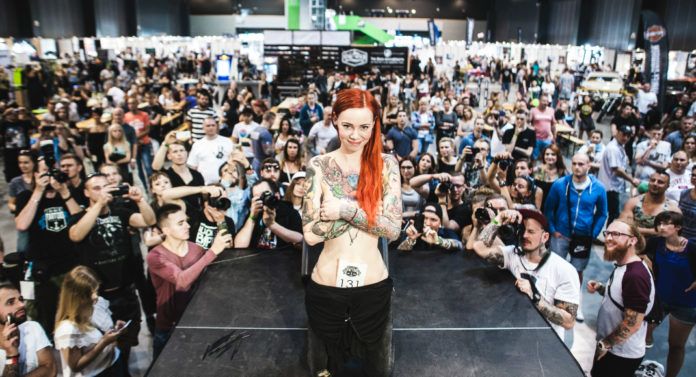 Dziewczyna w tatuażach stojąca na scenie, dookoła ludzie