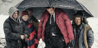 Grupa ludzi ubrana w kurski, stojąca pod dużym parasolem, dookoła pada śnieg