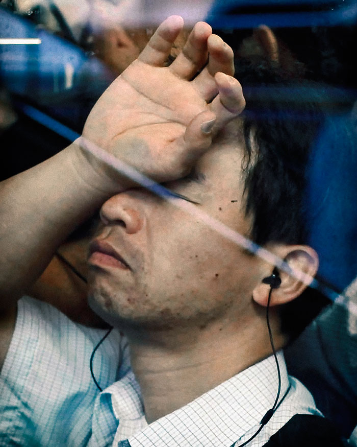 Mężczyzna siedzący w metrze, trzymający rękę na twarzy
