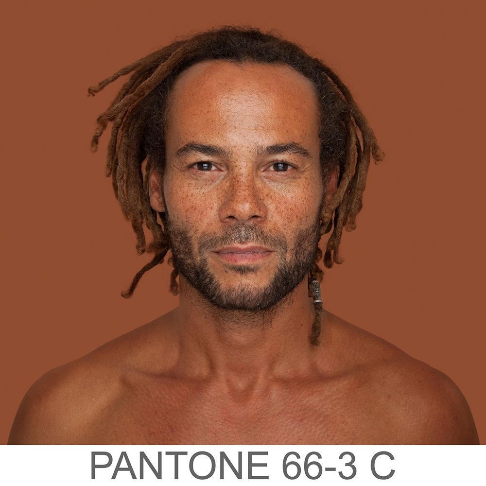 Fotografia portretowa kolorowa ukazująca mężczyznę o jasno-brązowym odcieniu skóry, drobnych dreadach i zaroście